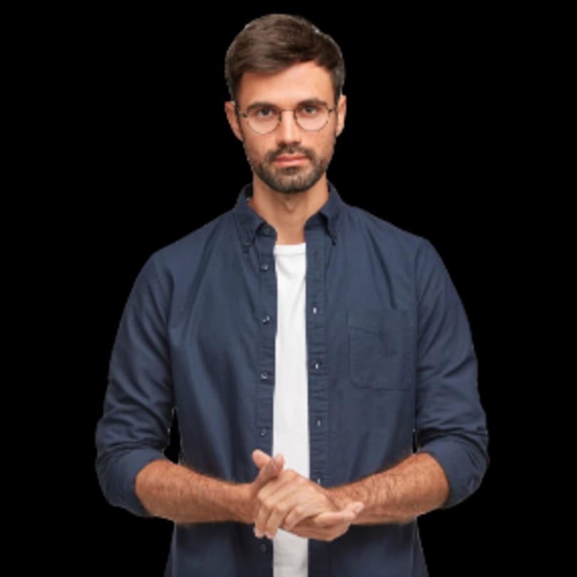 A man with glasses and a beard, wearing a blue shirt, stands with hands clasped.