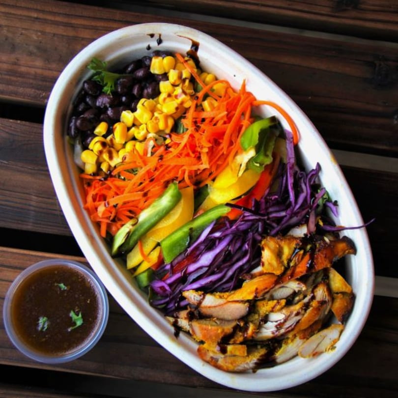 A colorful Mr.Cone Shawarma bowl with chicken, black beans, corn, shredded carrots, peppers, and red cabbage.