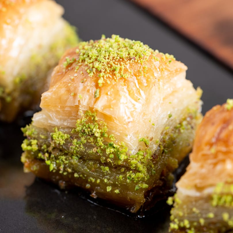 Close-up of three pieces of baklava, glistening with syrup and topped with crushed pistachios.