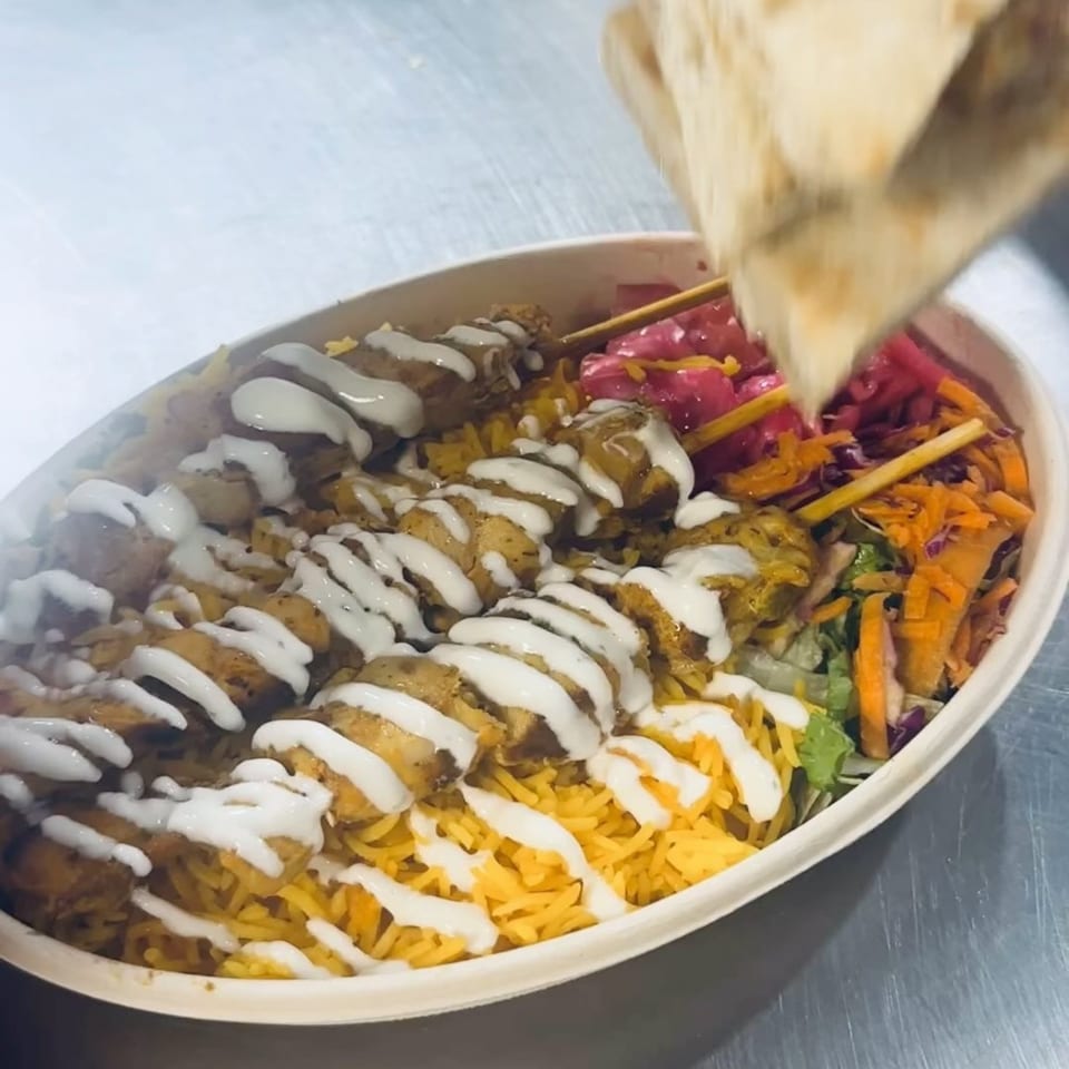 A Mr.Cone Shawarma bowl with chicken skewers, rice, pickled vegetables, and white sauce.