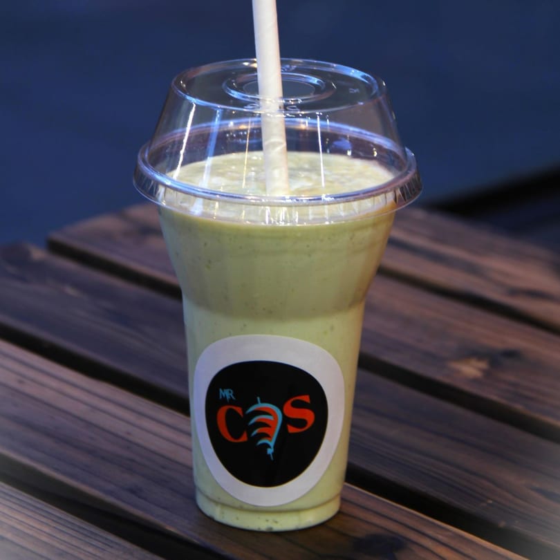 A Mr.Cone Shawarma green smoothie with a straw, on a wooden table.