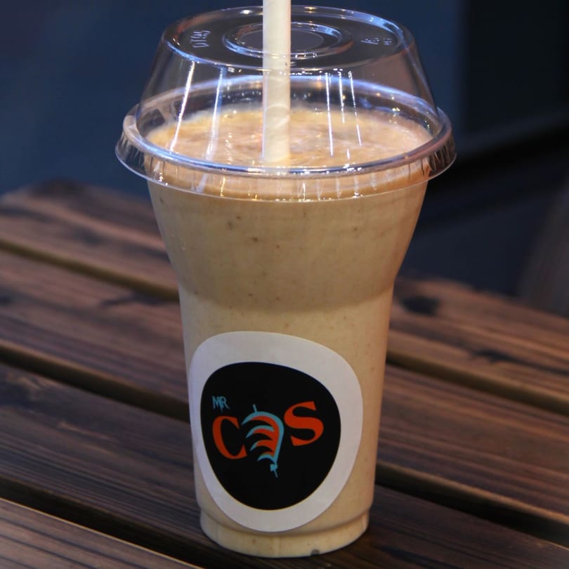 A Mr. Cone Shawarma smoothie in a clear cup with a straw, on a wooden table.